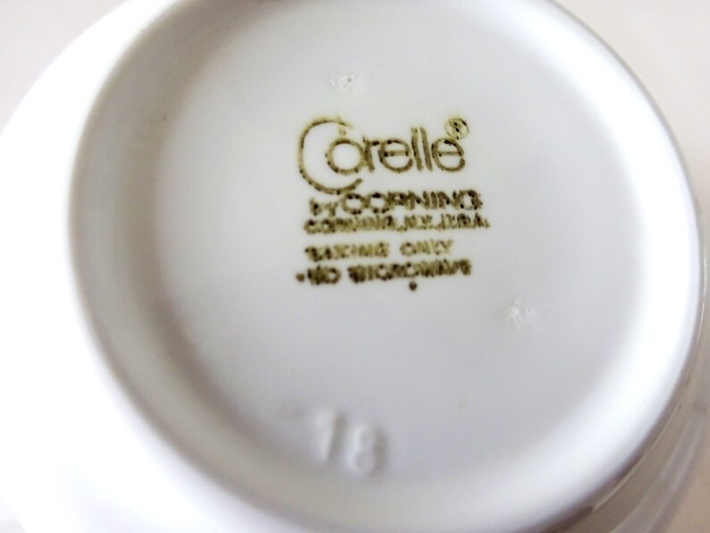 May include: A white ceramic bowl with a gold "Corelle" logo and the text "by Corning, Corning, NY, USA.  Oven Only - No Microwave."  The number "18" is printed on the bottom of the bowl.
