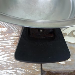 May include: A stainless steel cooking pot featuring a wide, polished metal rim and a black, heat-resistant handle. The handle is securely attached to the side of the pot with a visible metal screw and features the embossed text "S&H" on its surface.