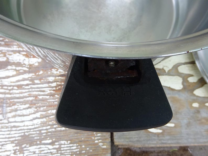 May include: A stainless steel cooking pot featuring a wide, polished metal rim and a black, heat-resistant handle. The handle is securely attached to the side of the pot with a visible metal screw and features the embossed text "S&H" on its surface.