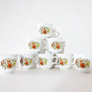 May include: Set of eight white ceramic mugs with a floral pattern in shades of orange, yellow, and green. The mugs are arranged in a pyramid shape.