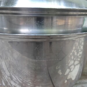 May include: A silver-toned stainless steel cooking pot with a matching lid. The pot features engraved text on the side that reads Regal, 18-8, STAINLESS STEEL, and the lid features engraved text that reads Pana-ease, 3 PLY, 18-8, STAINLESS STEEL.