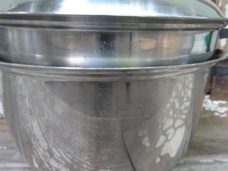 May include: A silver-toned stainless steel cooking pot with a matching lid. The pot features engraved text on the side that reads Regal, 18-8, STAINLESS STEEL, and the lid features engraved text that reads Pana-ease, 3 PLY, 18-8, STAINLESS STEEL.