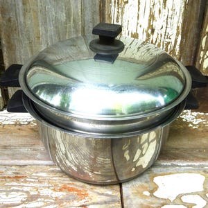 May include: A stainless steel stockpot with a matching lid and black heat-resistant handles on both sides. The pot features a polished metallic finish, a rounded body, and a secure-fitting lid with a central black knob for easy handling.