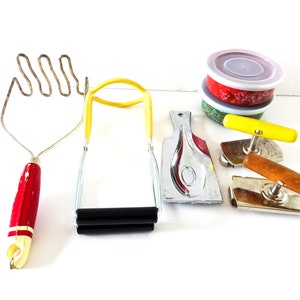 May include: A set of vintage kitchen tools including a red and yellow potato masher, a yellow and black spring-loaded tong, a silver spoon rest, two can openers with wooden handles, and a set of three red, green, and white nesting bowls with lids.