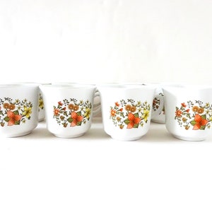 May include: Set of six white ceramic coffee mugs with a floral pattern in shades of orange, yellow, and green.