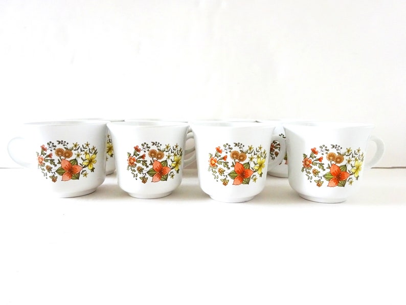 May include: Set of six white ceramic coffee mugs with a floral pattern in shades of orange, yellow, and green.