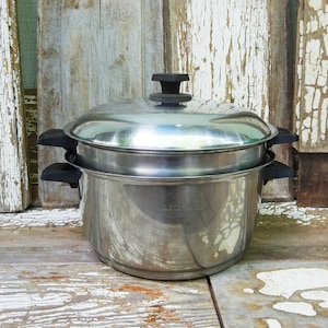 May include: A stainless steel double boiler pot set featuring a large base pot and a smaller insert pot. The set includes a matching stainless steel lid with a black knob. Both the base pot and the insert pot have black handles on each side.