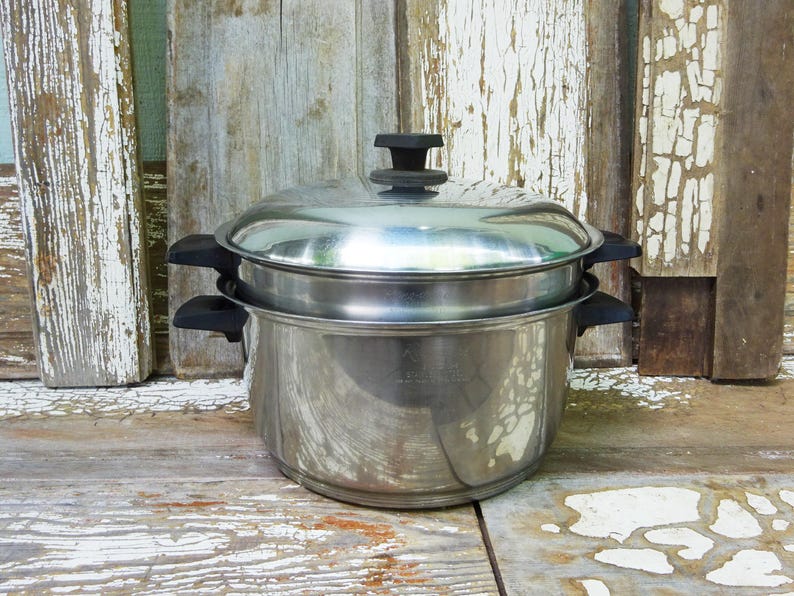 May include: A stainless steel double boiler pot set featuring a large base pot and a smaller insert pot. The set includes a matching stainless steel lid with a black knob. Both the base pot and the insert pot have black handles on each side.