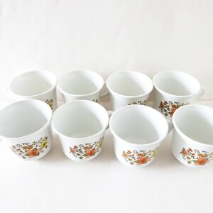 May include: Set of eight white ceramic mugs with a floral pattern in shades of orange, yellow, and green.