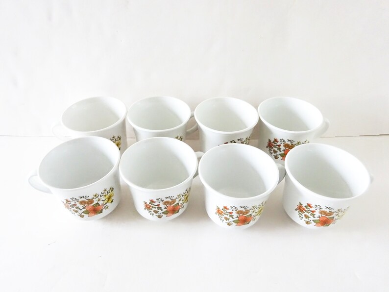 May include: Set of eight white ceramic mugs with a floral pattern in shades of orange, yellow, and green.
