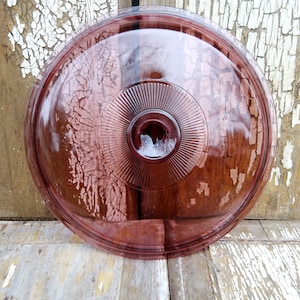 May include: A vintage glass lid with a deep purple hue and a raised, concentric circle design. The lid has a small hole in the center.