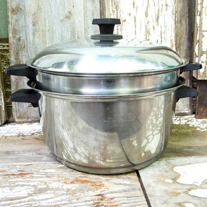May include: A stainless steel double boiler pot set featuring a large base pot and a smaller insert, both with black plastic side handles. The set includes a matching stainless steel lid with a black plastic knob handle on top.