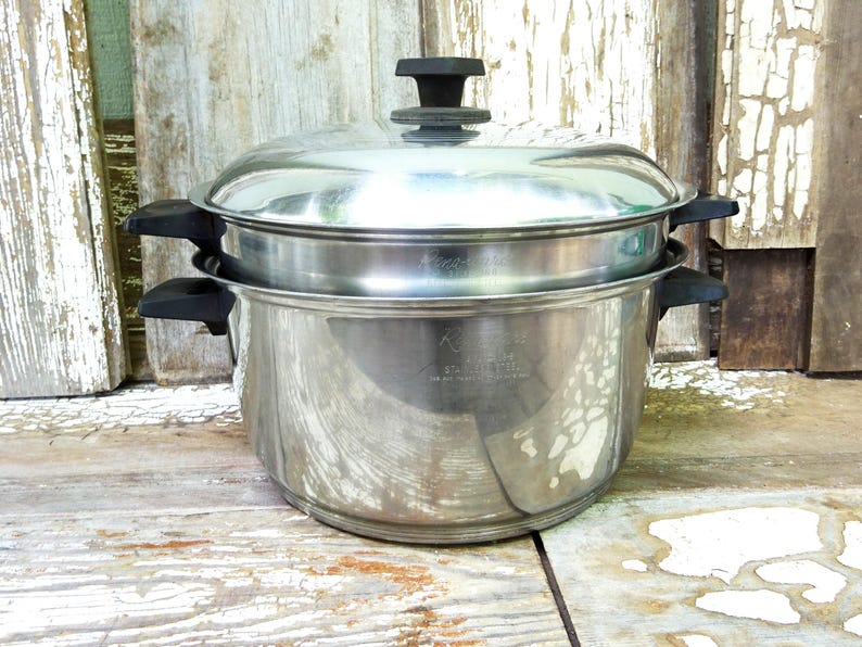 May include: A stainless steel double boiler pot set featuring a large base pot and a smaller insert, both with black plastic side handles. The set includes a matching stainless steel lid with a black plastic knob handle on top.