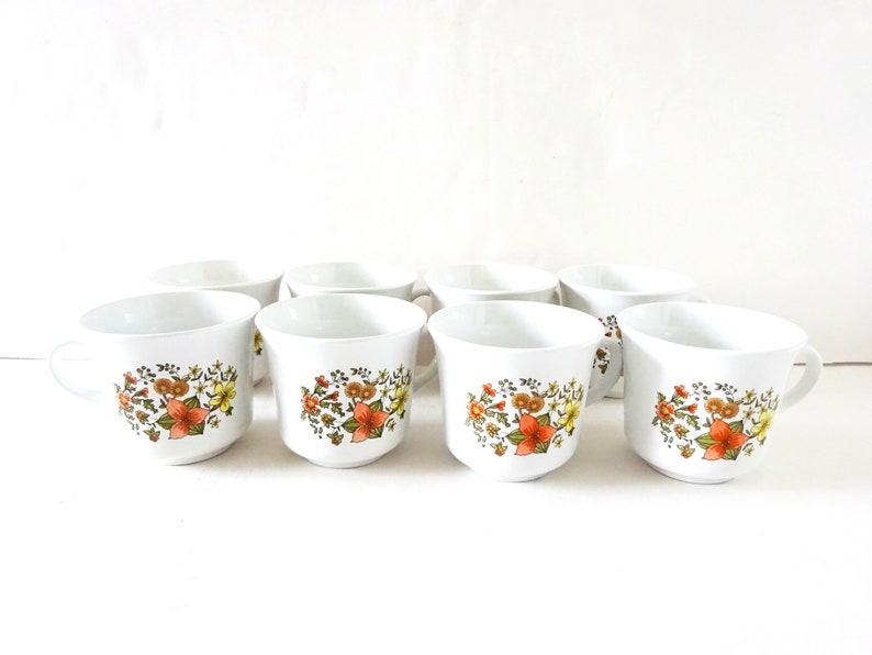 May include: Set of eight white ceramic mugs with a floral pattern in shades of orange, yellow, and green.
