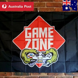 Könnte beinhalten: Eine schwarze rechteckige Flagge mit einer großen roten Raute in der Mitte, in der der weiße Text GAME ZONE steht. Unter dem Text sind zwei grüne monsterartige Klauen abgebildet, die einen weißen und grauen Videospiel-Controller halten.
