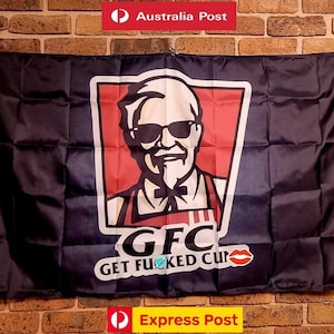 Peut inclure: Un drapeau rectangulaire noir présentant un graphique central d'un homme aux cheveux blancs, avec un bouc et des lunettes de soleil noires dans un trapèze rouge. Sous le graphique, le texte indique GFC GET FUCKED CUNT avec une icône de lèvres rouges.