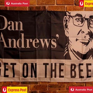 May include: A rectangular flag featuring a black and white graphic portrait of Dan Andrews wearing glasses. The text "Dan Andrews'" appears on the left, and the phrase "GET ON THE BEERS" is printed in large black capital letters along the bottom.