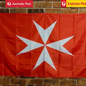 May include: A rectangular flag featuring a vibrant red background with a large, centred white Maltese cross. The flag has a white vertical strip along the left side with two metal grommets for hanging, displaying a classic eight-pointed cross design.