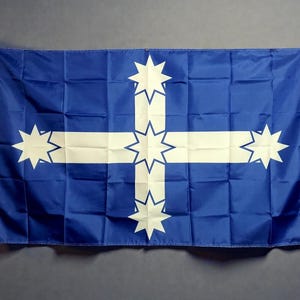 Könnte beinhalten: Eine rechteckige blaue Flagge mit einem großen weißen Kreuz, das aus fünf achtstrahligen Sternen besteht. Die Sterne befinden sich in der Mitte und an jedem Ende der Kreuzarme. Die Flagge hat einen weißen vertikalen Streifen mit Metallösen.