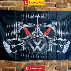 May include: A rectangular black flag featuring a large, stylised graphic of a gas mask in white and grey tones. The mask design includes two prominent red vertical stripes across the eye lenses and a Volkswagen logo on the central filter area.