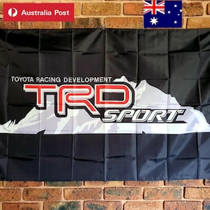 以下が含まれることがあります： 黒い長方形の旗。白い文字で「TOYOTA RACING DEVELOPMENT」、その下に赤と白の大きな「TRD」ロゴと白い「SPORT」の文字がデザインされている。黒い布地の上には、文字とロゴの背後に白い山のグラフィックが描かれている。