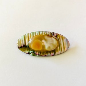 May include: An oval-shaped shell with a green, iridescent finish and a light brown centre. The shell has a smooth, polished surface.