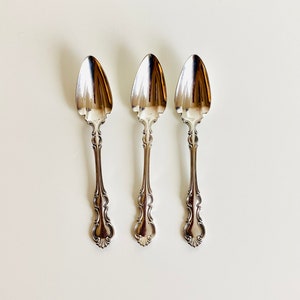 May include: Three silver spoons with ornate handles and a rounded spoon head.