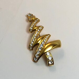 May include: A gold-toned Christmas tree brooch with clear rhinestones. The tree is made of twisted metal and has a stylized design.