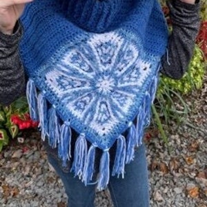 Könnte beinhalten: Ein blaues Häkelponcho mit einem weißen Schneeflockenmuster und Fransen. Das Poncho ist aus weichem Garn gefertigt und hat eine bequeme Passform.