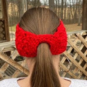 May include: Red knitted headband with a ponytail hole in the back. The headband has ear coverings.