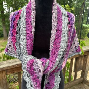 May include: A crocheted shawl with a gray and purple ombre design. The shawl is draped over a black dress form.