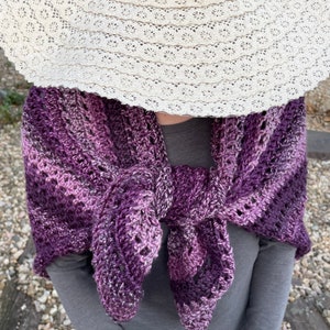 May include: A purple and white crocheted shawl with a lacy pattern. The shawl is draped over a person's shoulders and tied at the neck.
