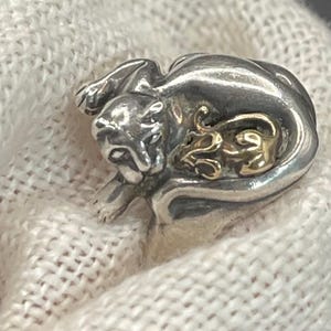 May include: A silver-toned metal ring featuring a sculpted panther or large cat figure with a smaller, gold-toned metal mouse or rodent figure nestled against its side. The metal surfaces are polished and reflective, showing detailed animal features.