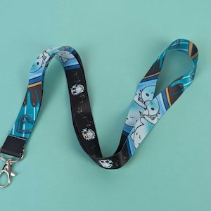 Könnte beinhalten: Ein blaues und schwarzes Lanyard mit einem Cartoon-Charakter-Design. Das Lanyard hat an einem Ende einen silbernen Clip.
