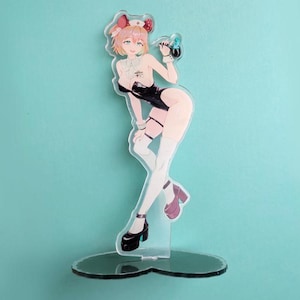 May include: A clear acrylic figure of an anime-style character in a black bodysuit, white stockings, and high heels. The character has pink hair and is holding a small object. The figure is on a clear, heart-shaped base.