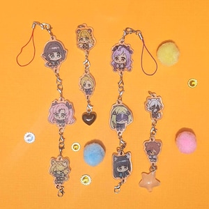 Puede incluir: Cuatro llaveros con colgantes de estilo anime con varios diseños de personajes, incluyendo un colgante de corazón y estrella. Los llaveros están sobre un fondo naranja brillante con pequeños elementos decorativos y pompones.