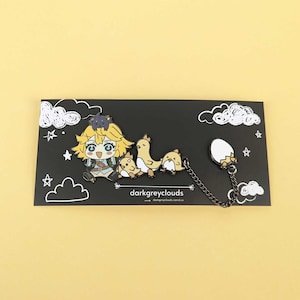 May include: A black enamel pin set featuring a cartoon character with yellow hair, three chick-like creatures, and a cracked egg. The pin set is connected by a chain and rests on a black card with white cloud and star illustrations. The text "darkgreyclouds.com" is visible.