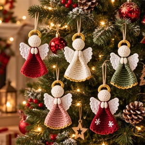 May include: Five handmade crochet angel ornaments hanging on a Christmas tree. Each angel features a round cream head, a yellow halo, white wings, and a dress in red, white, sage green, or dusty pink. One red dress has two white snowflake motifs.