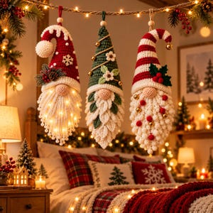 May include: Three hanging crochet gnome ornaments with pointed hats. The left gnome has a red hat with a white snowflake and lights in its beard. The center gnome has a green hat with flowers. The right gnome has a red and white striped hat.