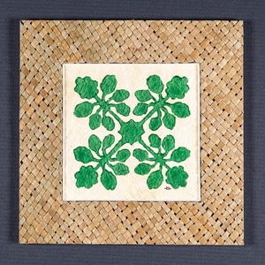 May include: A green floral design is framed in a woven, light brown mat. The design is made of four green leaves, each with a central stem and four smaller leaves. The design is symmetrical and centered in the mat.