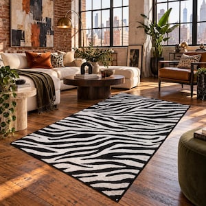 Op de afbeelding: Een rechthoekig vloerkleed met een contrastrijk zwart-wit zebrastrepenpatroon. Het kleed heeft een strakke afgewerkte rand en ligt plat op een houten vloer, met een herhalend organisch dierenprintontwerp over het gehele oppervlak.