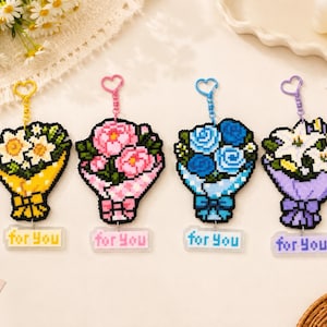 May include: Four pixel art style flower bouquet keychains with heart-shaped clasps. Each features a unique color scheme: yellow with daisies, pink with peonies, blue with roses, and purple with lilies. Each has a small tag reading for you.