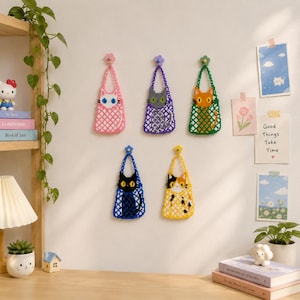 May include: Five small, rectangular, beaded wall hangings, each featuring a different cat design in a mesh-like pattern. The cats are white, grey, orange, black, and calico, suspended from colourful flower-shaped hooks on a plain wall.