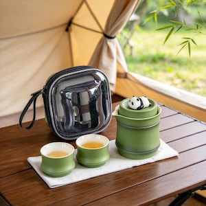 May include: A green ceramic tea set featuring a teapot with a panda figurine on the lid, two matching tea cups, and a clear zippered carrying case. The teapot and cups have a smooth, matte finish and a bamboo-inspired cylindrical shape.