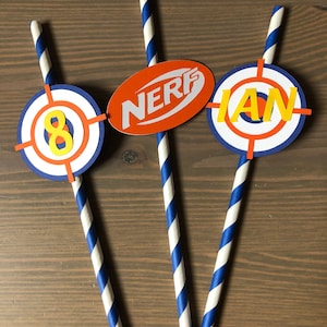 May include: Three blue and white striped paper straws with orange and white target-shaped paper circles attached. The circles have the words "NERF", "8", and "IAN" in yellow letters.
