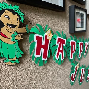 May include: A green and red paper banner with the words "Happy Birthday Justin" on it. A cartoon character of Lilo from Lilo and Stitch is on the left side of the banner.