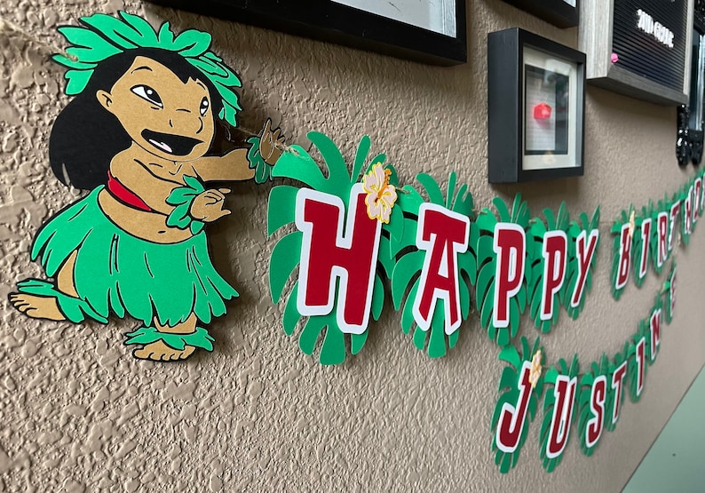 May include: A green and red paper banner with the words "Happy Birthday Justin" on it. A cartoon character of Lilo from Lilo and Stitch is on the left side of the banner.