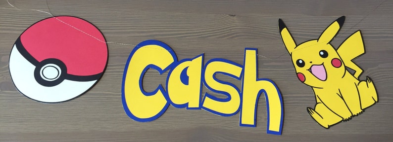 May include: A yellow and blue banner with the name "Cash" in large, stylized letters. The banner is decorated with a red and white Pokeball on the left and a yellow cartoon Pikachu on the right.