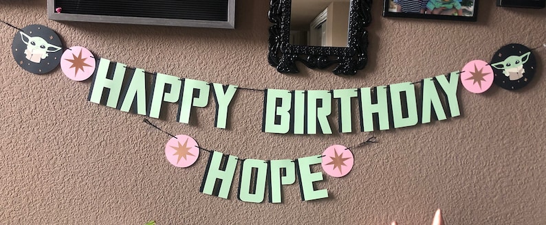Pode incluir: Uma faixa verde e preta com as palavras "Happy Birthday Hope" e decora&ccedil;&otilde;es de estrelas rosa e douradas. A faixa apresenta um personagem de desenho animado da franquia Star Wars.