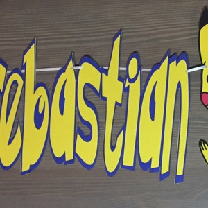 May include: A yellow and blue banner with the name "Sebastian" in bold, yellow letters. A red and white Pokeball is on the left and a yellow cartoon Pikachu is on the right.
